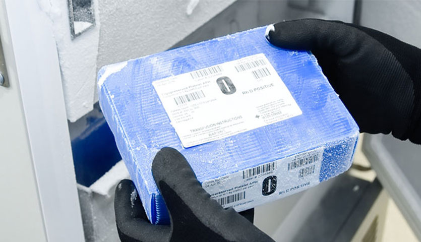 a blue frozen blood box is being taken out of a freezer by a scientist wearing gloves and a gown