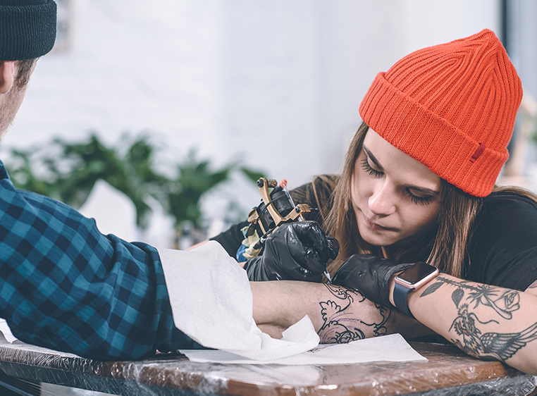 a woman is tattooing a man's arm