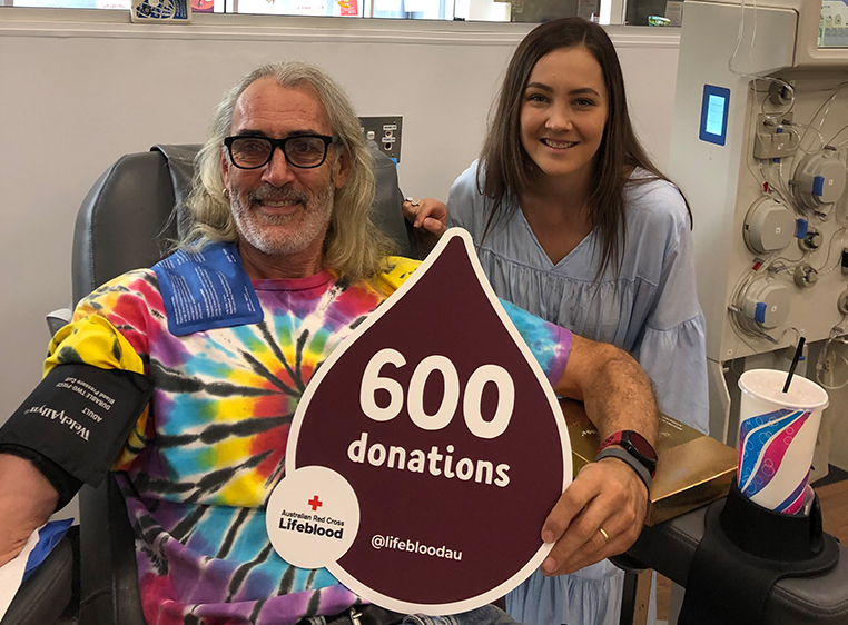 photo of donor Bruce and recipient Taylor smiling and holding a sign with 600 donations written on it