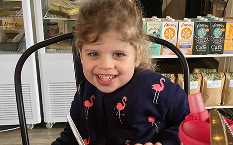 girl smiling at camera wearing a jumper with flamingos seated in a cafe