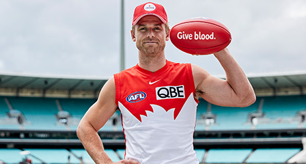 sydney swan dane rampe holding a football with give blood written on it