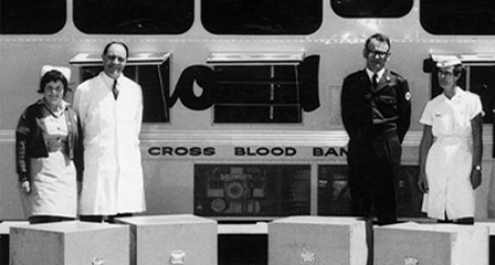 black and white photo of nurses and doctors standing in front of a red cross donation bus