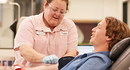 a male about to donate blood while a nurse assists