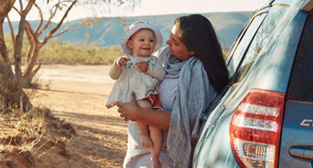 a mother holding her baby outside next to a car