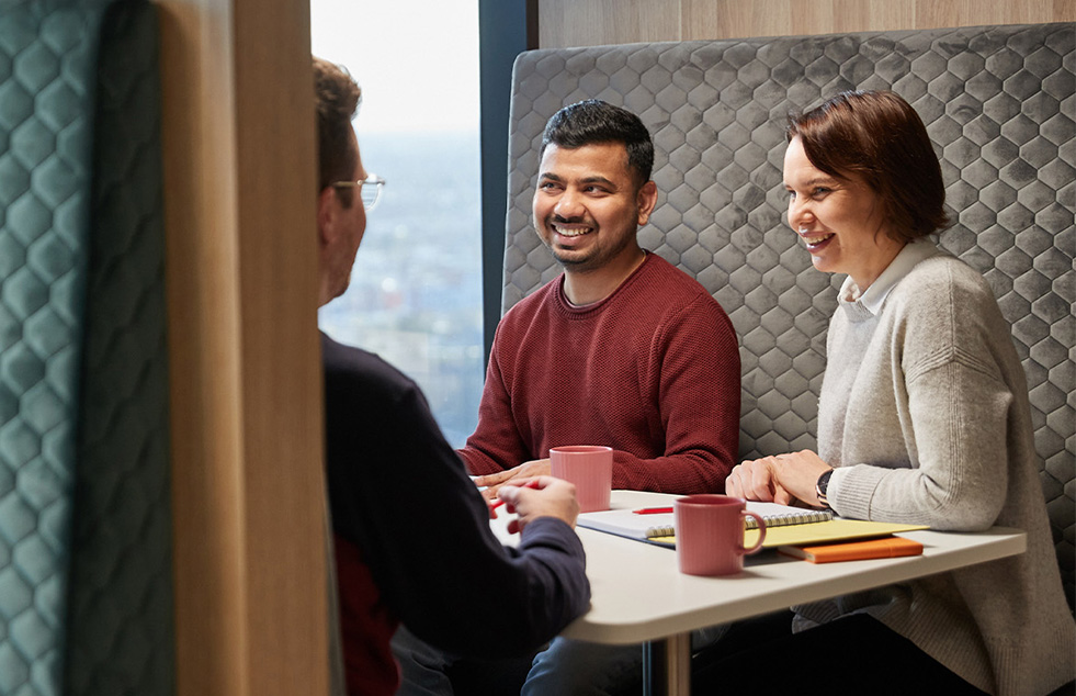 three people seated at a table in an office chatting and smiling