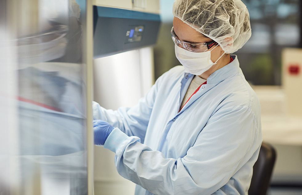 a scientist wearing a hair net, goggles, mask, blue lab coat and gloves