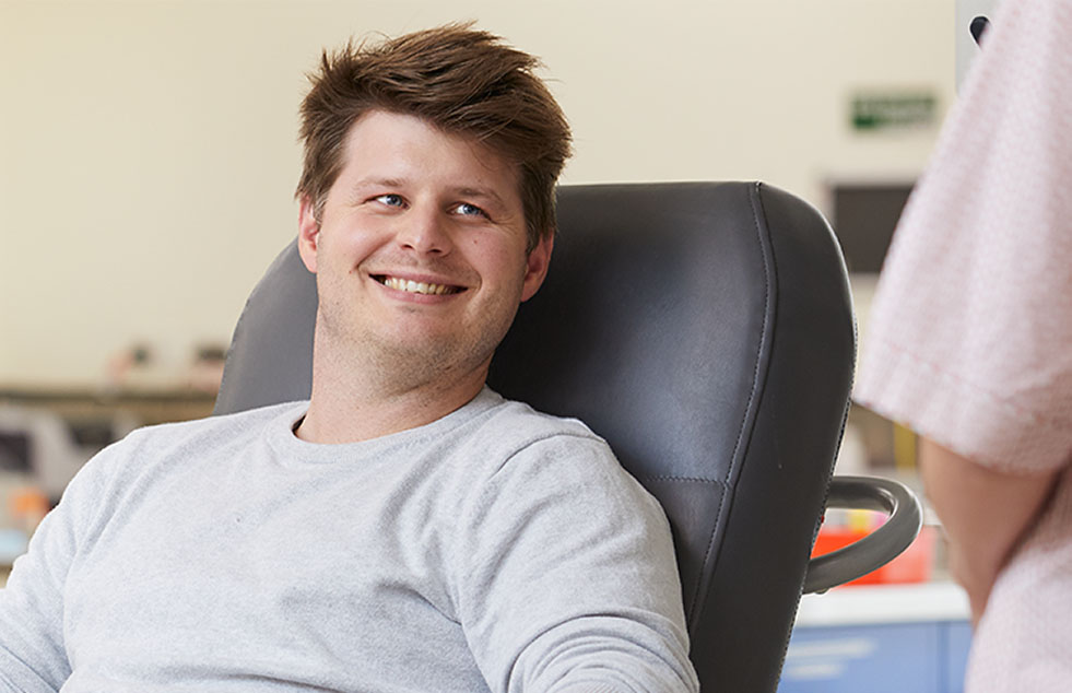 a male about to donate blood while a nurse assists