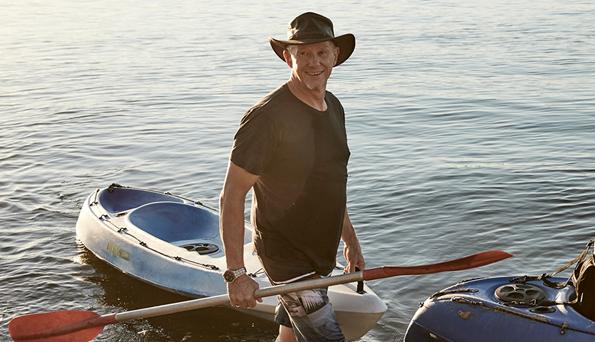 Man carrying paddle in front of kayak floating on water