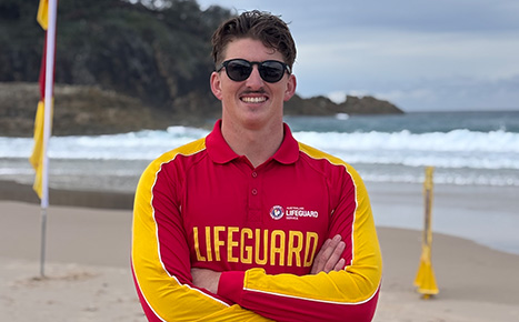 Image of a young male in his 30s working as a lifeguard with the ocean behind him