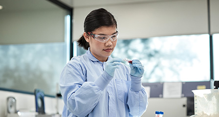 image of scientist wearing blue lab coat and safety glasses inspecting a test tube