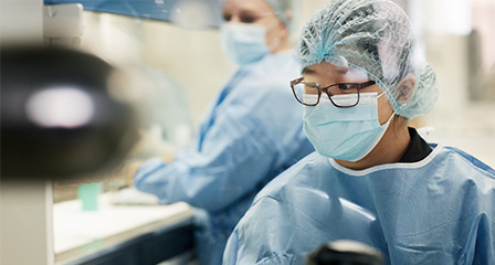 scientist in blue lab coat wearing face mask and safety glasses