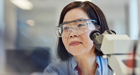 a scientist wearing goggles and blue lab coat in front of a microscope