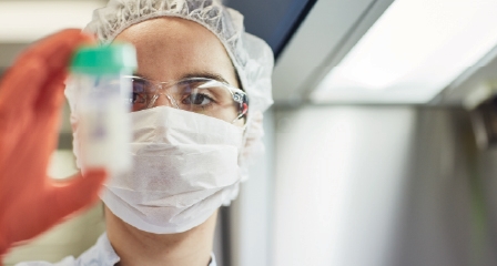 a person wearing mask and gloves holding a sample bottle