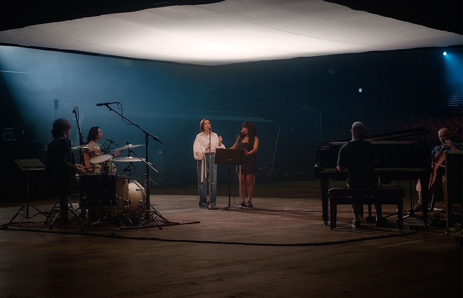 a band playing instruments on stage with tina arena and ngaiire singing into microphones
