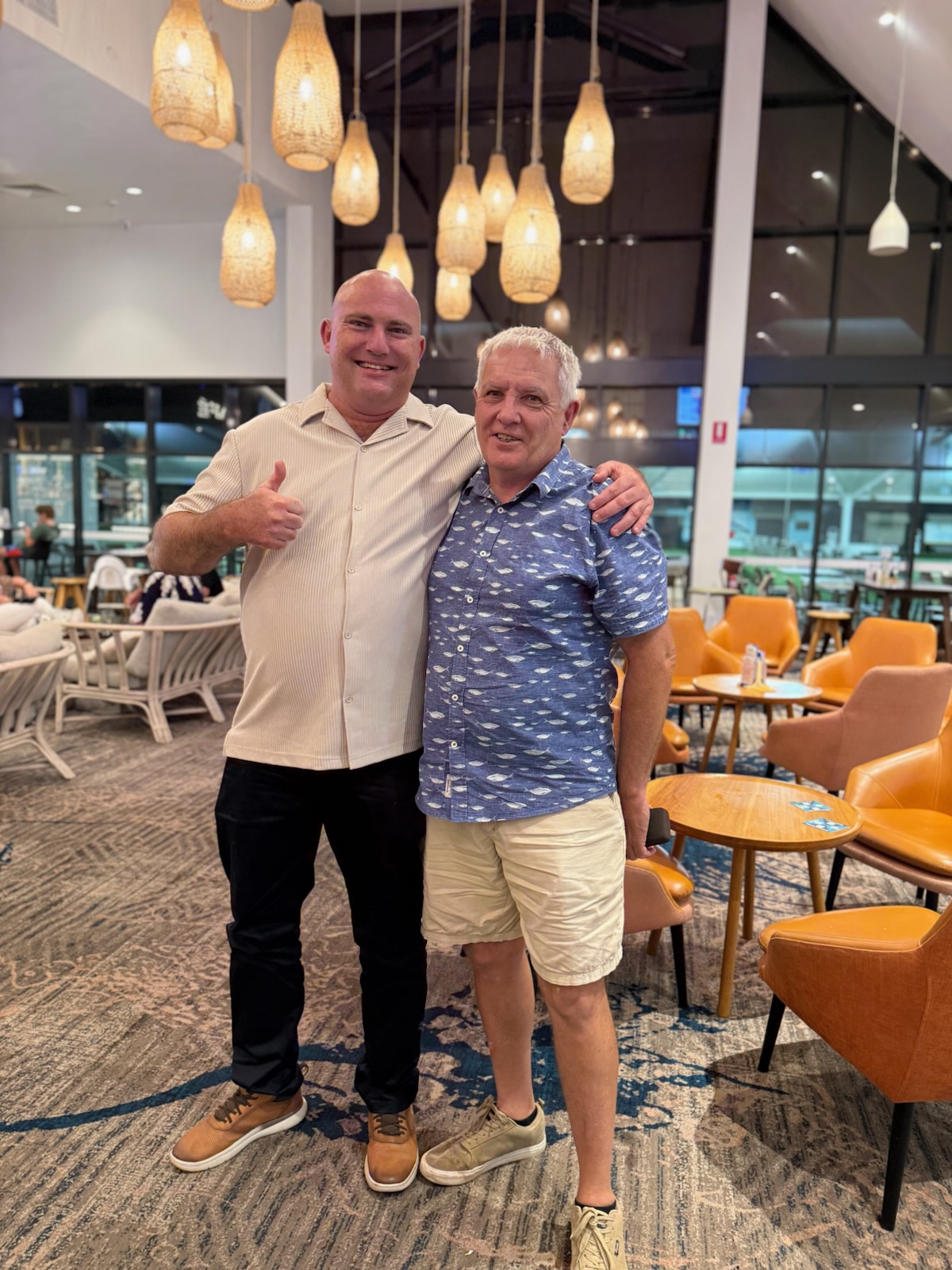 Image of two males smiling at the camera and one holding up a thumbs up sign