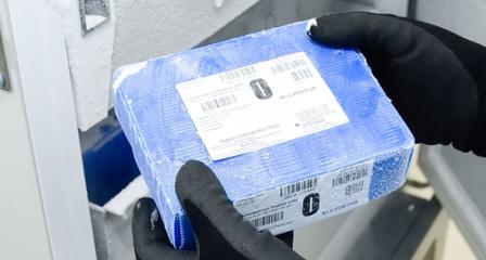 a blue frozen blood box is being taken out of a freezer by a scientist wearing gloves and a gown