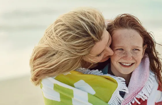 a mother and daughter on a beach with towels over their shoulders