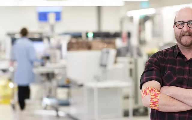 photo of artist Geoff Nees looking at the camera with his arms crossed, on his right elbow is the bandage he designed
