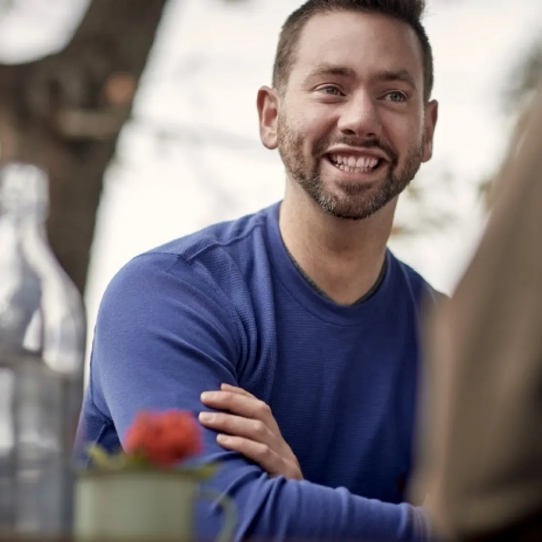 a man seated at a cafe table smiling and talking with someone