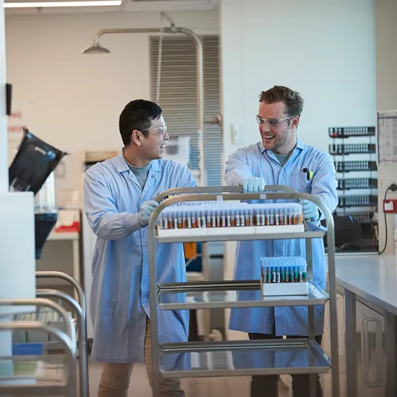 two scientists in a lab pushing a trolley of test tubes