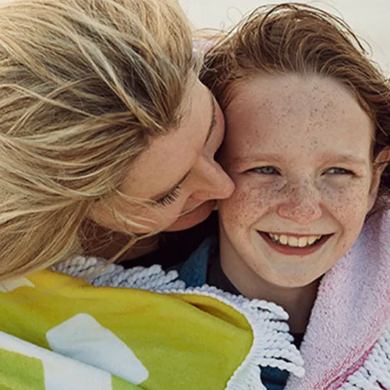 a mother and child on a beach smiling with a beach towel over their shoulders