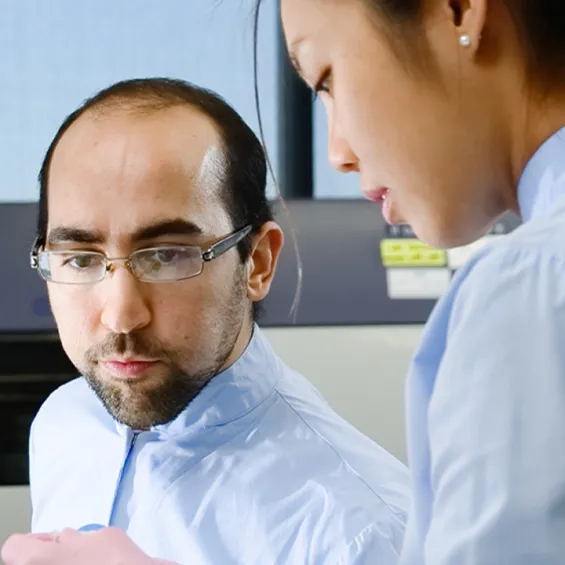 two scientists are working together at a desk with technical equipment behind them