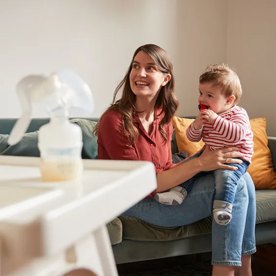 a woman and baby smiling and a milk pump on a table in the foreground