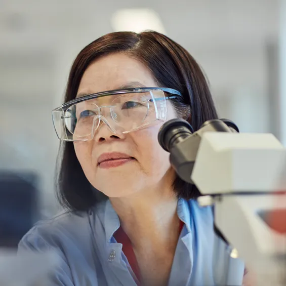 a scientist wearing goggles and blue lab coat in front of a microscope