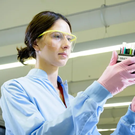 a scientist wearing goggles and gloves is holding up a rack of test tubes