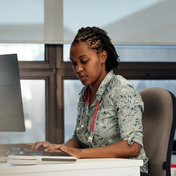 image of woman sitting at desk with stethoscope around neck in front of a computer
