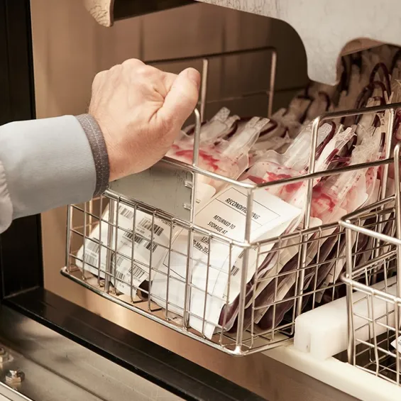 a hand picking up blood bags in a storage rack