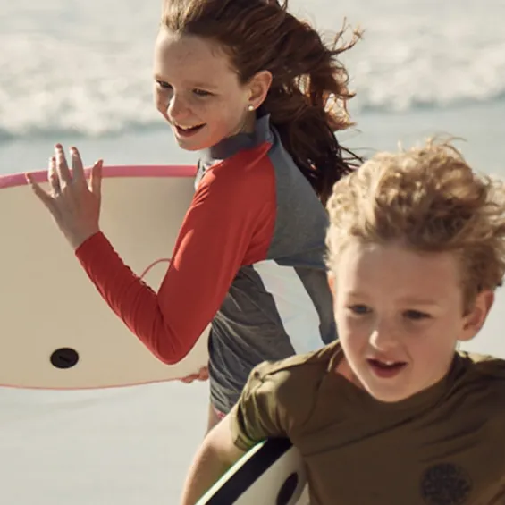 two kids running on the beach holding bodyboards