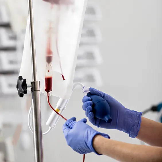 image of blood transfusion set up with gloved hands holding tube
