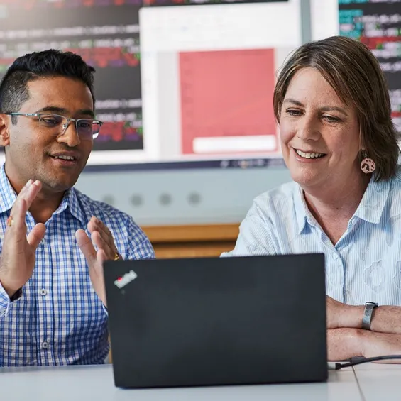 two people talking at a desk with a laptop in front of them