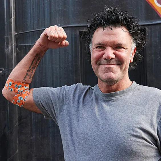 a photo of artist blak douglas smiling and holding his right arm up in a flex pose, around his elbow is the bandage he designed