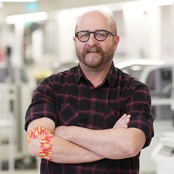 photo of artist geoff nees looking at the camera and folding his arms, around his right elbow he is wearing the bandage he designed