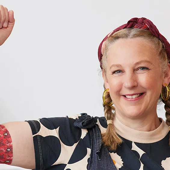 photo of artist Madeleine Stamer smiling at the camera with her right hand raised, around her elbow is the bandage with her design