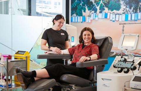 a donor is seated in a chair and smiling while a nurse prepares the donation