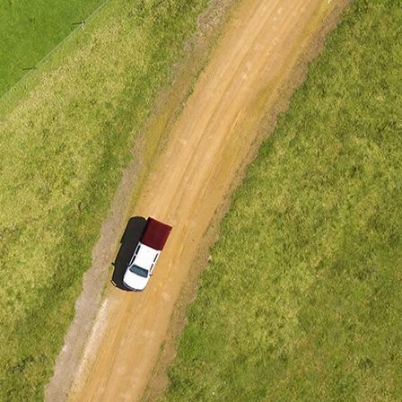 aerial photo of a field with a car driving on a dirt road through it