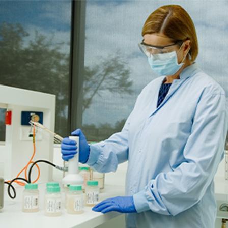 scientist wearing coat, gloves, face mask and goggles working at a table with containers of donated breastmilk