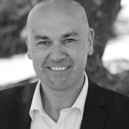 headshot of man smiling to camera with trees in the background