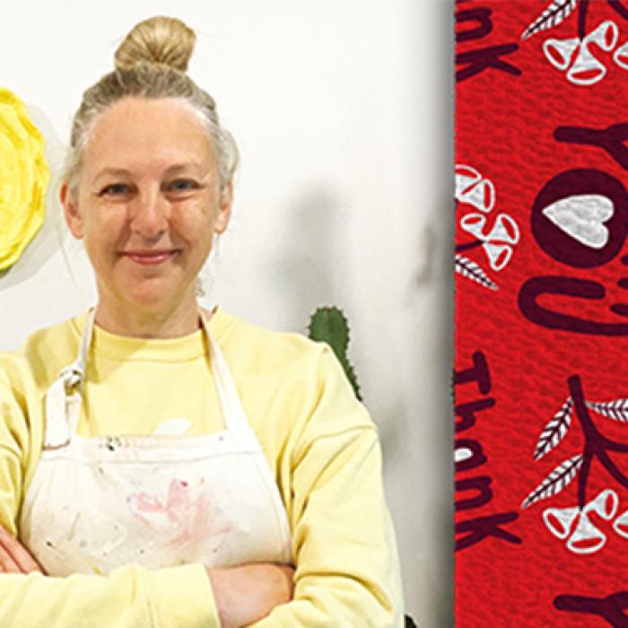 photo of artist Madeleine Stamer wearing an apron and facing the camera with her arms crossed, on the right is her design of the words thank you on a red background and a branch motif